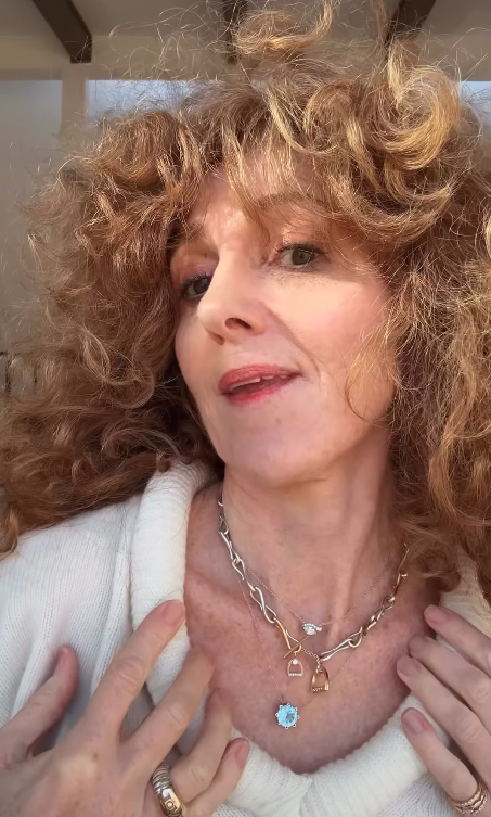 Woman with curly hair wearing a necklace with a blue pendant and silver and gold chain equestrian necklace. 