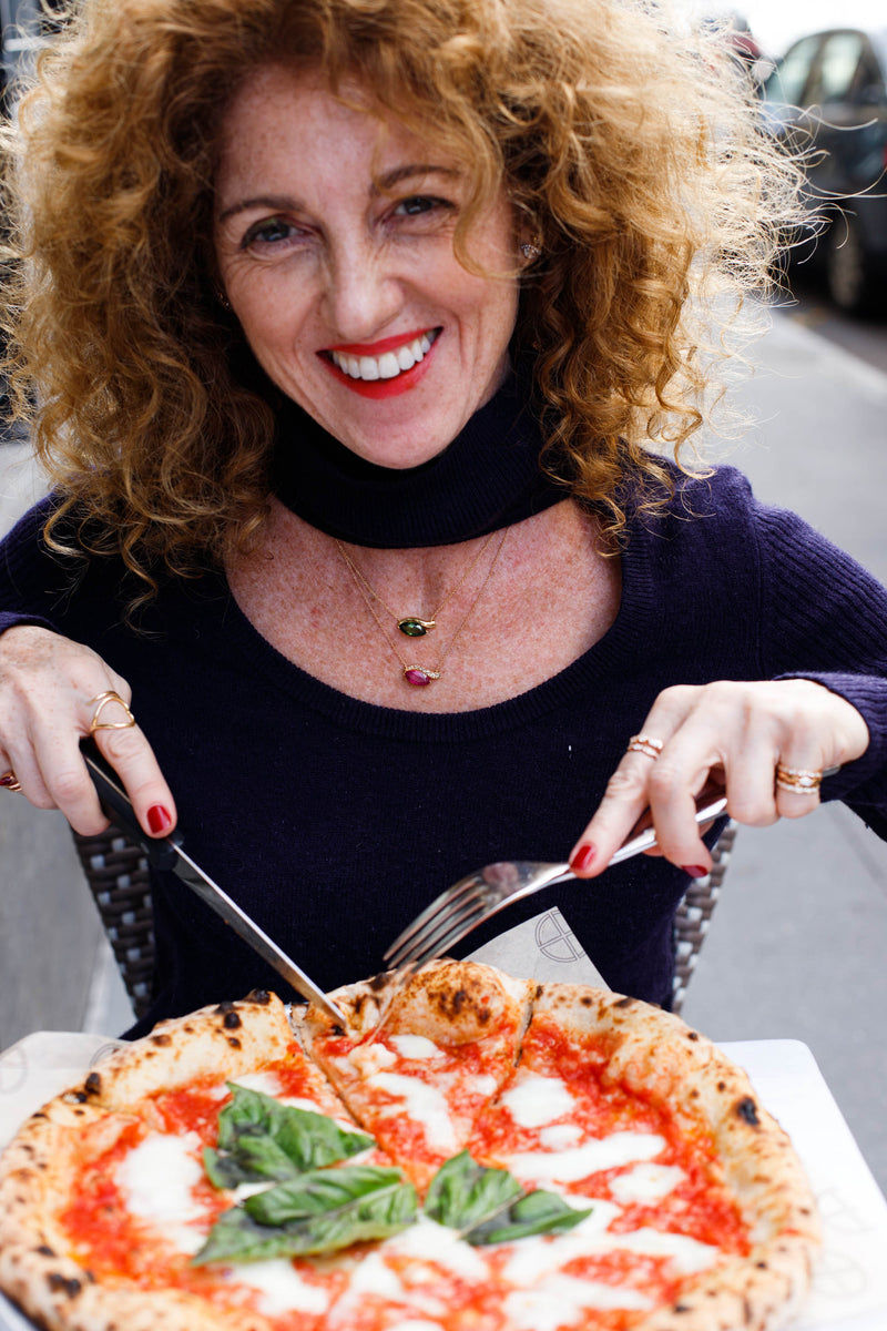 Woman with curly hair and red lipstick holding a pizza with a knife and fork.