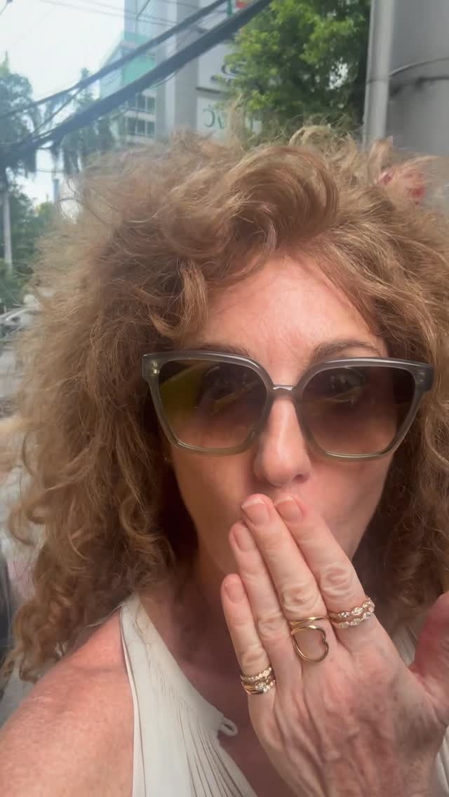 Person with curly hair wearing sunglasses and rings, outdoors.