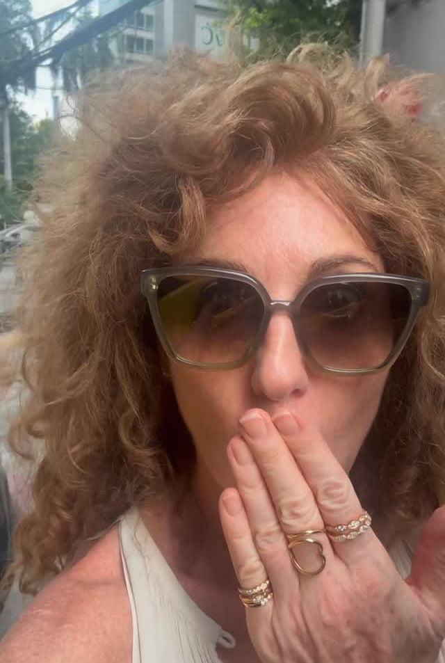 Person with curly hair wearing sunglasses and rings, outdoors.